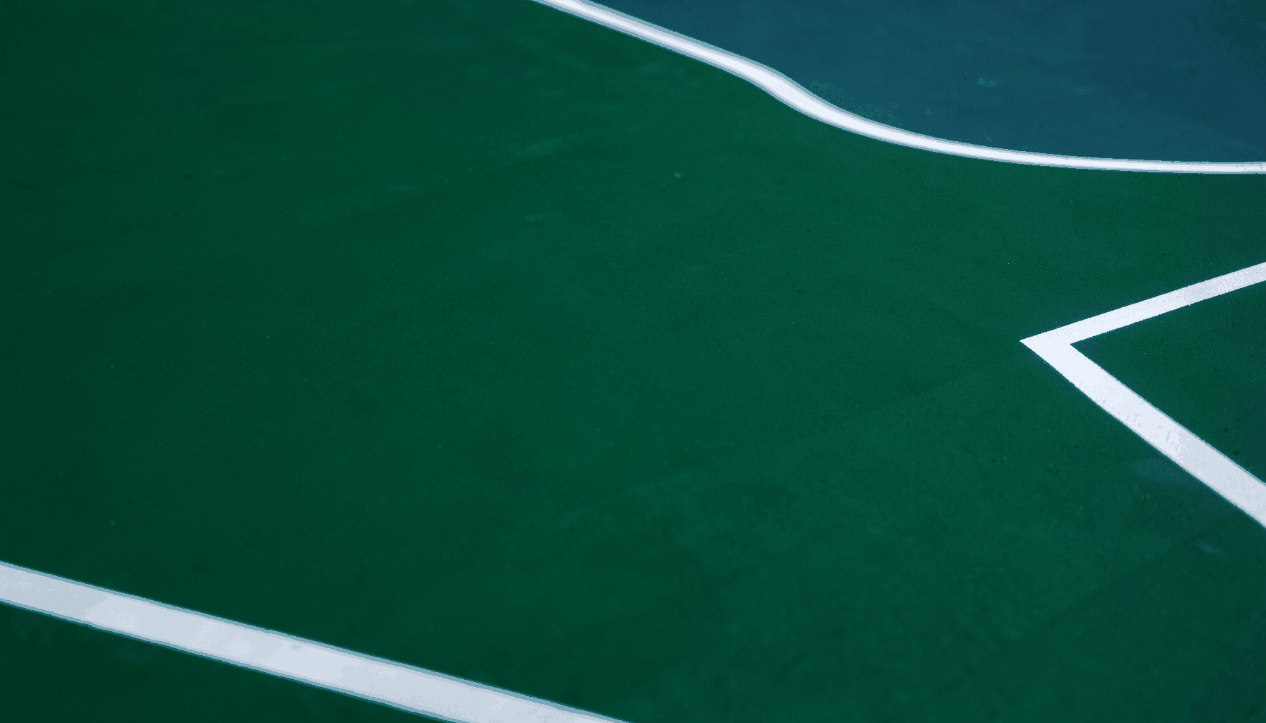 Close-up of a deep green acrylic sports court surface with crisp white boundary lines, showing the smooth matte texture